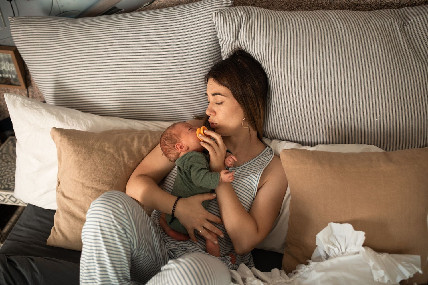 Mother tenderly holding her newborn while relaxing in a cozy bedroom setting, capturing a moment of warmth and care.